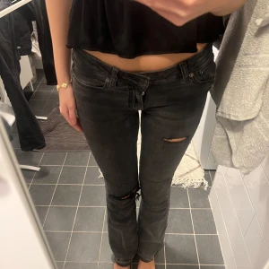 Lågmidjade jeans  - Säljer ett par svarta lågmidjade bootcut jeans från Junkyard med slitna detaljer vid knäna. Materialet är jeans i bomull och de har en snygg, mörk tvätt som passar till allt.