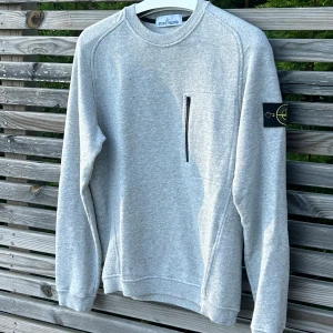 Grå sweatshirt från Stone Island - Säljer en grå sweatshirt från Stone Island med klassisk patch på ärmen. Tröjan har rund hals, långa ärmar och är gjord i mjuk bomull. I bra skick 7,5/10 