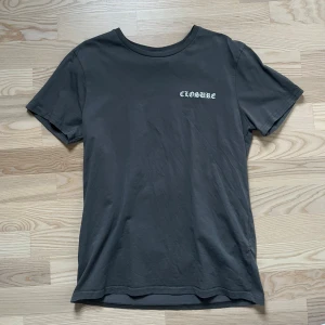 Mörkgrå CLOSURE t-shirt med tryck - Snygg mörkgrå t-shirt från Closure med vit text på bröstet och stort grafiskt tryck på ryggen. Trycket på ryggen visar flera 'CLOSURE'-texter och en staty i svartvitt. Klassisk passform och rund hals. Perfekt för dig som gillar streetwear vibes. Köpt på Zalando 