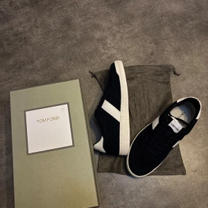 Svarta sneakers från Tom Ford - Snygga svarta sneakers från Tom Ford med vita detaljer och vit sula. Skorna har en klassisk låg profil, snörning och är tillverkade i mocka och skinn. Perfekta för dig som gillar stilrena och exklusiva sneakers med en sportig touch.