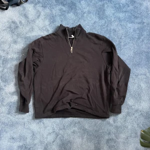 Svart half zip tröja från Weekday - Svart långärmad tröja från Weekday med hög krage och half zip-dragkedja. Tröjan är i bomull och har en clean, enkel look som passar perfekt till jeans eller cargobyxor. Ribbad krage och muddar ger en snygg och bekväm passform.