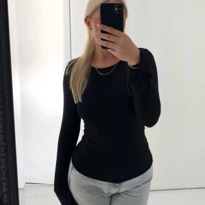 Svart långärmad topp från Gina Tricot - En svart, basic långärmad topp från Gina Tricot i storlek S. Modellen är figurnära med rund halsringning och tillverkad i mjuk bomull. Plagget har en slits längst ut i ärmarna. För referens är jag 164cm