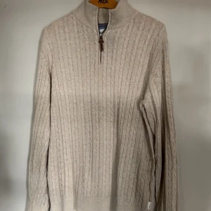 Beige kabelstickad tröja S - Snygg beige kabelstickad tröja med relaxed fit. Tröjan har hög krage och half zip-dragkedja med läderdetalj. (Storlek S men passar även M)