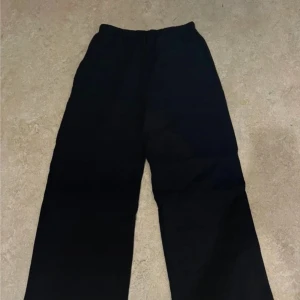 Svarta vida byxor från H&M - Svarta byxor från H&M med elastisk midja och raka, vida ben. Byxorna är tillverkade i ett lätt och mjukt tyg som ger en avslappnad känsla. Perfekta för dig som gillar en loose och bekväm stil.