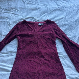 Vinröd spetströja från Dry Lake - Supersnygg vinröd tröja från Dry Lake med v-ringning och långa utsvängda ärmar. Tröjan är täckt av blommig spets och har dragkedja i ryggen. Perfekt för dig som vill sticka ut med en elegant och trendig look.