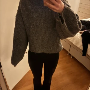 Grå stickad tröja från Gina Tricot - Mysig grå stickad tröja från Gina Tricot i croppad modell. Tröjan har breda, långa ärmar. 