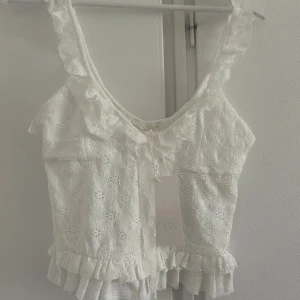 Vit spetsig linnetopp från Zara - Superfin vit linnetopp från Zara med spetsdetaljer och volang längs axelband och nederkant. Toppen är ärmlös och kort i modellen. Söt broderad struktur och passar till både jeans och kjol. Aldrig använd och säljer då den inte passade mig som har en väldigt lång överkropp💗💗