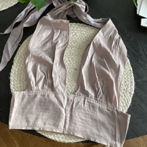 Ljuslila halterneck topp från SHEIN - Säljer en ljuslila croppad halterneck topp från SHEIN i storlek M. Toppen har breda knytband i nacken och en djup v-ringning framtill. Tillverkad i ett mjukt och lätt material som känns skönt mot huden.