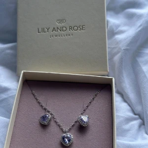 Halsband med hjärtformade stenar Lily and Rose - Supersött halsband från Lily and Rose med tre hjärtformade hängen i ljuslila och silver. Kedjan är tunn och elegant, och stenarna glittrar snyggt i ljuset. Perfekt accessoar för att lyfta vilken outfit som helst.