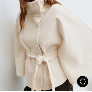 Poncho/cape jacka  - Kollar endast intresse🌞Cape jacka med knytskärp i midjan. Kappan är vit och har långa, vida ärmar. Den har oversize fit, hög krage och knappar upptill. Från Gina tricot med lapp kvar! Strl XS/S