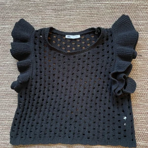 Svart stickad topp med volang från Zara - Svart stickad topp från Zara med genombrutet mönster och stora volangärmar. Modellen är croppad och ärmlös men jätte bekväm. Funkar till alla tillfällen. Vid intresse och/eller frågor skriv!