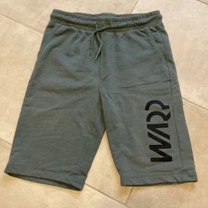Gröna shorts från Warp - Hej! Jag säljer ett par snygga gröna shorts från Warp med svart tryck på ena benet. Modellen har elastisk midja med snörning och två sidofickor. Den är nopprig på baksidan och framsidan, men det påverkar inte så mycket. (Se bilder). Det finns också ett litet hål på baksidan. Perfekta för chill dagar med mys! Mjukt material i bomull för skön känsla!