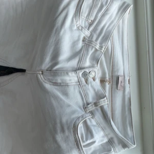 Vita bootcut jeans från Nelly - Säljer ett par vita Low waisted bootcut jeans från Nelly med snygga kontrastsömmar och dubbla knappar i midjan. Jeansen har klassiska fickor fram och bak, samt en cool detalj med broderad söm på bakfickorna. Perfekta att styla med en oversized hoodie eller crop top. Jag är 160 cm så jag har behövt att vika up dem lite, så de är små små fläckar längst ner som man typ inte ser