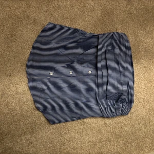 Blåvit randig tubb topp med knappar - Snygg blå och vit randig tubbtopp  med knappar framtill. Toppen har en avslappnad passform och bred linning upptill. Perfekt för dig som gillar en stilren och enkel look med en twist.