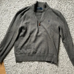 Grå half zip tröja Polo Ralph Lauren - Snygg grå tröja från Polo Ralph Lauren i 100% bomull. Klassisk ribbad krage och muddar, half zip-dragkedja och broderad logga på bröstet. Perfekt för lager-på-lager och chill stil. Långärmad och normal passform.
