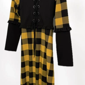 Svart och gul rutig långklänning - Unik långklänning med svart och gul rutigt mönster, snörning framtill och volangdetaljer vid ärmslut. Klänningen har långa ärmar och ett snyggt bälte som knyts i midjan. Perfekt för dig som gillar statement-plagg med coola detaljer.