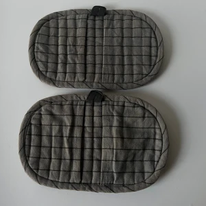 Grå rutiga grytvantar i bomull - Säljer ett par gråa grytvantar med svart rutmönster. De är rektangulära med rundade kanter och har en liten svart ögla för upphängning.