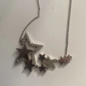 Silvrigt halsband med stjärnor - Ett snyggt halsband i silverfärg med flera stjärnor i olika storlekar. Några av stjärnorna är täckta av små glittrande stenar som ger extra bling. Kedjan är tunn och smidig, perfekt för att lyfta vilken outfit som helst. Från ioaku och nickelfri!