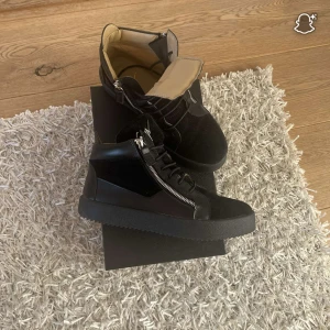 Svarta high top Giuseppe Zanotti med dragkedja  - Snygga svarta high top sneakers med både snörning och silverfärgade dragkedjor på sidorna. Skorna har en chunky platt sula och är tillverkade i en mix av skinn och mocka. Insidan är ljusbeige för en schysst kontrast. Perfekta för dig som gillar streetstyle.