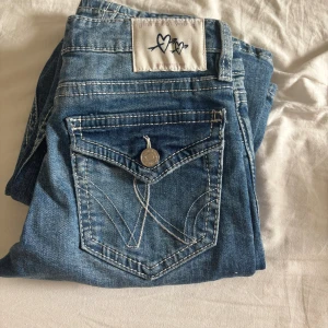 Blå bootcut jeans från Gina Tricot - Säljer ett par blå bootcut jeans från Gina Tricot med slitna detaljer framtill och snygga bakfickor med lock och knapp. Jeansen har normal passform och klassisk femficksdesign. Perfekta för dig som gillar en avslappnad och trendig look . Storlek är 152 från Gina Young 