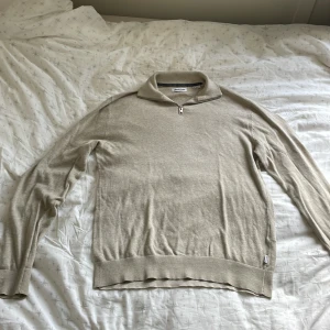 Beige half zip-tröja Jack & Jones S - Hej, nu säljer jag en beige långärmad tröja från Jack & Jones i storlek S. Tröjan har en klassisk half zip-dragkedja vid kragen och är stickad i mjukt material. Den har en tight passform men samtidigt stretchig vilket gör att den passar alla kropstyper. Den har visst slitage i ena armhålan.