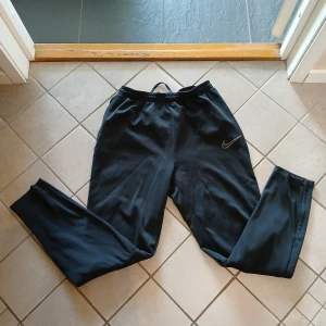 Svarta mjukisbyxor från Nike - Svarta mjukisbyxor från Nike med klassisk Swoosh-logga på låret. Byxorna har elastisk midja och är tillverkade i mjukt material som passar perfekt för chill eller träning. Snygg och enkel design som funkar till det mesta. Korta i storlek 