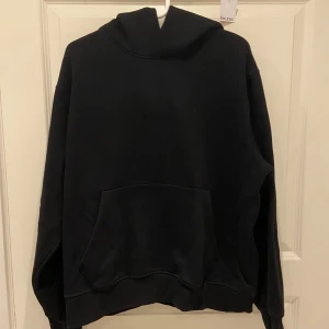 Svart hoodie från Jack & Jones - En klassisk svart hoodie från Jack & Jones med stor känguruficka framtill och huva. Tröjan är i mjuk bomullsblandning och har ribbade muddar vid ärmslut och nederkant. Perfekt för en avslappnad och stilren look.