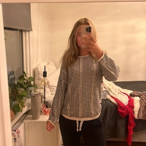 Svartvit stickad kofta från Pulz Jeans - Stickad kofta från Pulz Jeans i svart och vitt med rutigt mönster. Långärmad modell med knappar på sidan och rund halsringning. Mjuk och skön, perfekt för lager-på-lager. Snygga detaljer längs kanterna och avslappnad passform.