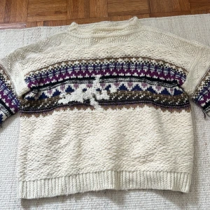 Isabel Marant stickad tröja  - Mysig beige stickad tröja med klassiskt flerfärgat mönster i lila, blått, brunt och vitt över bröstet och ärmarna. Tröjan har ribbade muddar och en avslappnad passform med lång ärm. Perfekt för kyliga dagar och ger en retrovibe till din outfit. Den är i storlek 42, men liten i storleken då jag har vanligtvis 34/36 och då blir den perfekt oversized!