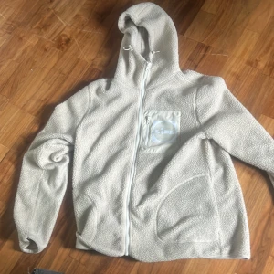 Lidl fleece - Mysig beige teddyjacka från Livergy med huva och hel dragkedja framtill. Jackan har en bröstficka med dragkedja och en stor Lidl-logga. Perfekt för kyliga dagar och riktigt skön att slänga på sig. Vet ej om den säljs längre
