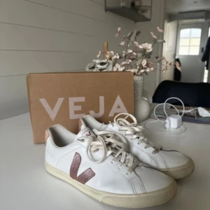 Veja Esplar Logo sneakers vit/rosa - Snygga Veja Esplar Logo sneakers i vitt skinn med ljusrosa detaljer och klassisk V-logga på sidan. Modellen har rund tå, platt sula och snörning. Perfekt för dig som gillar clean och stilren look med en touch av färg. Lite defekter på skosnörena men det går att bleka eller tvätta bort.
