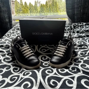  Dolce & Gabbana skor - Stilrena svarta sneakers från Dolce & Gabbana med vita snören och vit sula. Skorna har rund tå och är tillverkade i skinn med silvriga detaljer vid hälen. Perfekta för dig som vill ha en klassisk men lyxig look.