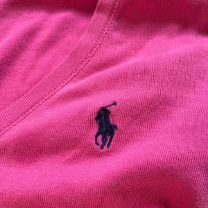 Rosa v-ringad t-shirt från Ralph Lauren - Snygg rosa t-shirt från Ralph Lauren Sport med v-ringning och klassisk broderad logga på bröstet. Modellen är kortärmad och gjord i mjuk 100% bomull, perfekt för dig som gillar stilrena och sportiga plagg med en färgklick.