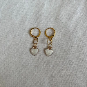 Örhängen  - Jag säljer ett par fina och söta örhängen i färgen guld, längst ner hänger det ett fint hjärta med lite vit blandad färg.🤍Passar perfekt nu när hösten och vintern kommer💕 Skicka ett meddelande om ni har några frågor eller prisförslag, allt är diskuterbart😊 Checka in min profil för att hitta fler fina saker!😌 