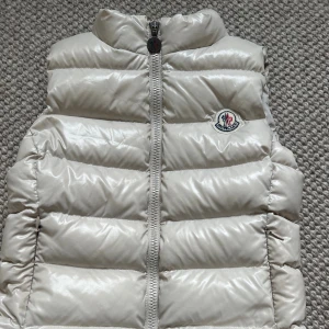 Beige dunväst från Moncler - Beige dunväst från Moncler med glansig finish och klassisk logga på bröstet. 