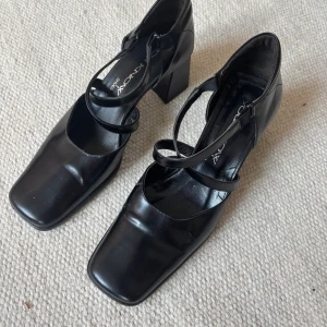 Svarta klackskor med remmar 39 - Stilrena svarta klackskor i skinn  med fyrkantig tå och bred klack. Skorna har dubbla tunna remmar över foten. Perfekta för dig som gillar en modern och edgy look. Helt nya! 