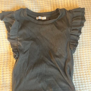 Svart croppad topp med volangärm Zara - Svart ribbad croppad topp från Zara med korta volangärmar. Snygg och enkel modell som sitter tight och har rund halsringning. 