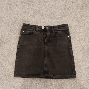 Svart jeanskjol från Cubus - Svart jeanskjol från Your Denim med klassisk femficksdesign, bälteshällor och dragkedja framtill. Rak modell i kort längd, perfekt till sneakers eller boots. Snygg och enkel att matcha med allt.