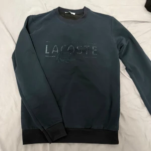 Mörkblå sweatshirt från Lacoste - Snygg mörkblå sweatshirt från Lacoste med broderad logga framtill. Tröjan har rund hals, ribbade muddar och är tillverkad i mjuk bomullsmix. Perfekt för dig som gillar stilren och sportig look.