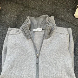 Grå stickad cardigan Gran Sasso (intressekoll) - Intressekoll på en snygg grå stickad kofta från Gran Sasso med hel dragkedja och ribbad hög krage. Tröjan har ärmar med förstärkta mockadetaljer på armbågarna och ribbade muddar. Tröjan är nyskick och har inga defekter. I storlek 48 men blivit lite mindre i tvätten så passar därav bättre som 46. Vilket motsvarar s-xs. 