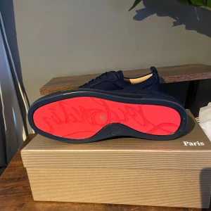 Mörkblå sneakers från Louboutin - Snygga mörkblå sneakers från Louboutin med klassisk röd sula och broderad logga på hälen. Skorna har rund tå, platt sula och är tillverkade i mocka med matchande mörkblå snörning. Perfekt för dig som gillar exklusiv och stilren design.