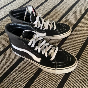 Svarta Vans Sk8-Hi sneakers - Säljer ett par klassiska Vans Sk8-Hi sneakers i svart mocka och canvas med vit sula och vit sidestripe. Skorna har snörning, hög modell och rund tå. Perfekta för dig som gillar streetstyle.