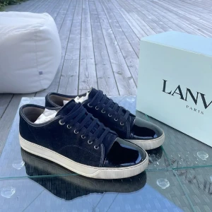 Lanvin sneakers i mörkblå mocka - Snygga sneakers från Lanvin i mörkblå mocka med lackad svart tå och vita sulor.  Skorna är i mycket fint skick med box. Dem är i storlek 43 och har mycket kvar att ge. Skriv vid intresse!!