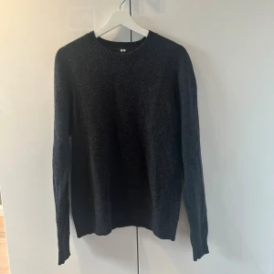 Mörkgrå stickad tröja från Uniqlo - Säljer en stilren mörkgrå stickad tröja från Uniqlo i storlek L. Tröjan har rund halsringning, långa ärmar och ribbade muddar. Perfekt för lager-på-lager och passar till det mesta i garderoben.