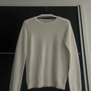Vit stickad tröja med struktur - Säljer en vit stickad tröja från Weekday med snygg struktur och rund halsringning. Tröjan har långärmade ärmar och ribbade muddar vid ärmslut och nederkant. Perfekt för lager-på-lager och enkel att matcha med jeans eller kjol.
