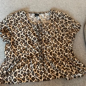 Leopardmönstrad blus med snörning - Säljer en kortärmad blus från Gina Tricot med leopardmönster i bruna och svarta toner. Blusen har snörning framtill, volang nertill och en lös passform. 