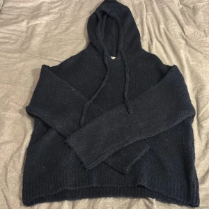 Svart stickad hoodie från Gina Tricot - Mysig mörkblå stickad hoodie från Gina Tricot med huva och snörning. Tröjan har långärmade ärmar och en loose passform som gör den extra chill. Perfekt för kalla dagar när du vill vara både bekväm och snygg.