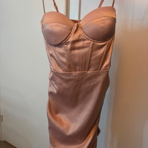 Champagnefärgad satin klänning från SHEIN - Supersnygg kort klänning i champagnefärgad/rosa satin från SHEIN. Klänningen har figurnära passform, reglerbara smala axelband och markerad byst med kupor. Baksidan har en snygg rynkdetalj och dragkedja. 