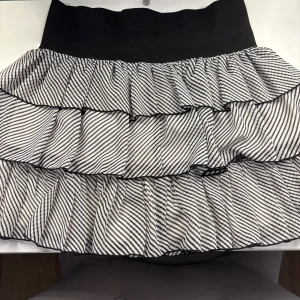 Randig volangkjol i svartvitt, stl 36 - Supersöt kort volangkjol med svartvitt randigt mönster och bred svart midja. 