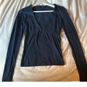 Mörkblå långärmad v-ringad topp - En stilren mörkblå topp med lång ärm och djup v-ringning. Snygg passform som sitter nära kroppen och passar perfekt till jeans eller kjol. Enkel och tidlös design som är lätt att matcha med olika outfits.